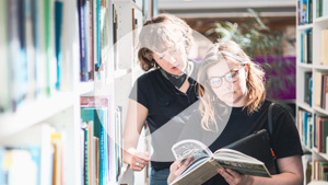 Studenter står och läser böcker vid bokhylla på universitetsbiblioteket